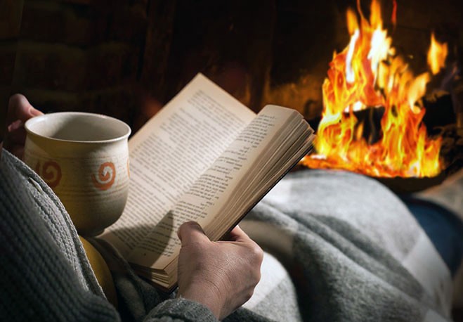 женщина отдыхает с чашкой горячего чая и книгой перед камином